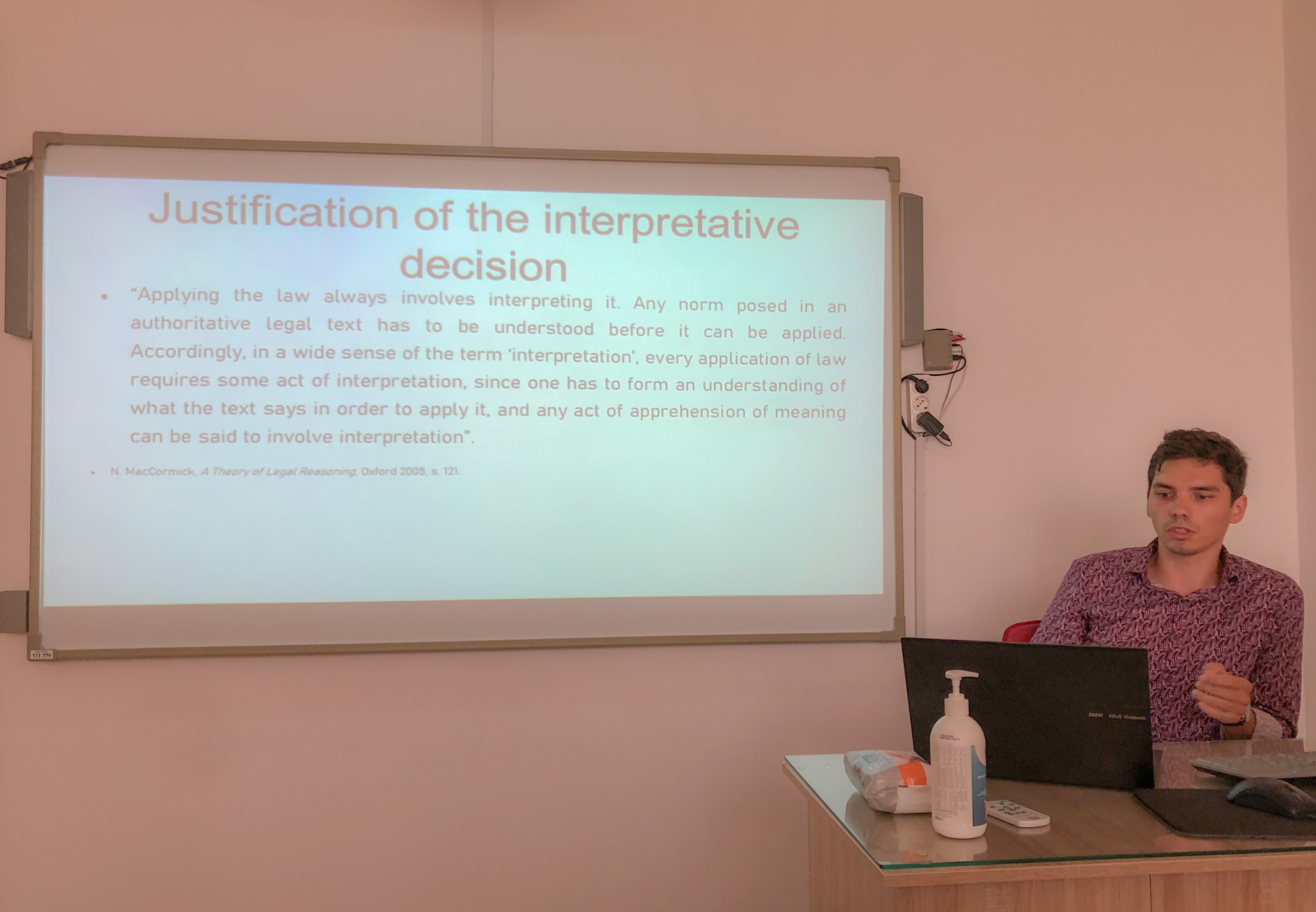 mgr Michał Wieczorkowski podczas wystąpienia (w pozycji siedzącej, prezentujący slajd "Justification of the interpretative decision")